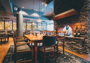 A restaurant interior with wooden tables and chairs, stone walls, and hanging pendant lights.