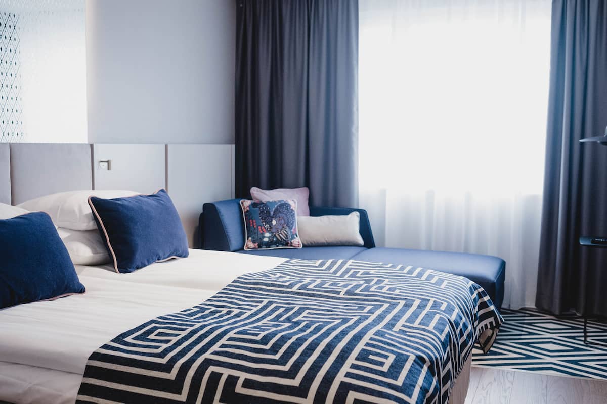 A modern hotel room with a large bed, a bedside table, and a window with curtains.