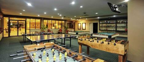 A room with multiple foosball tables, pool tables, and a billiards table.