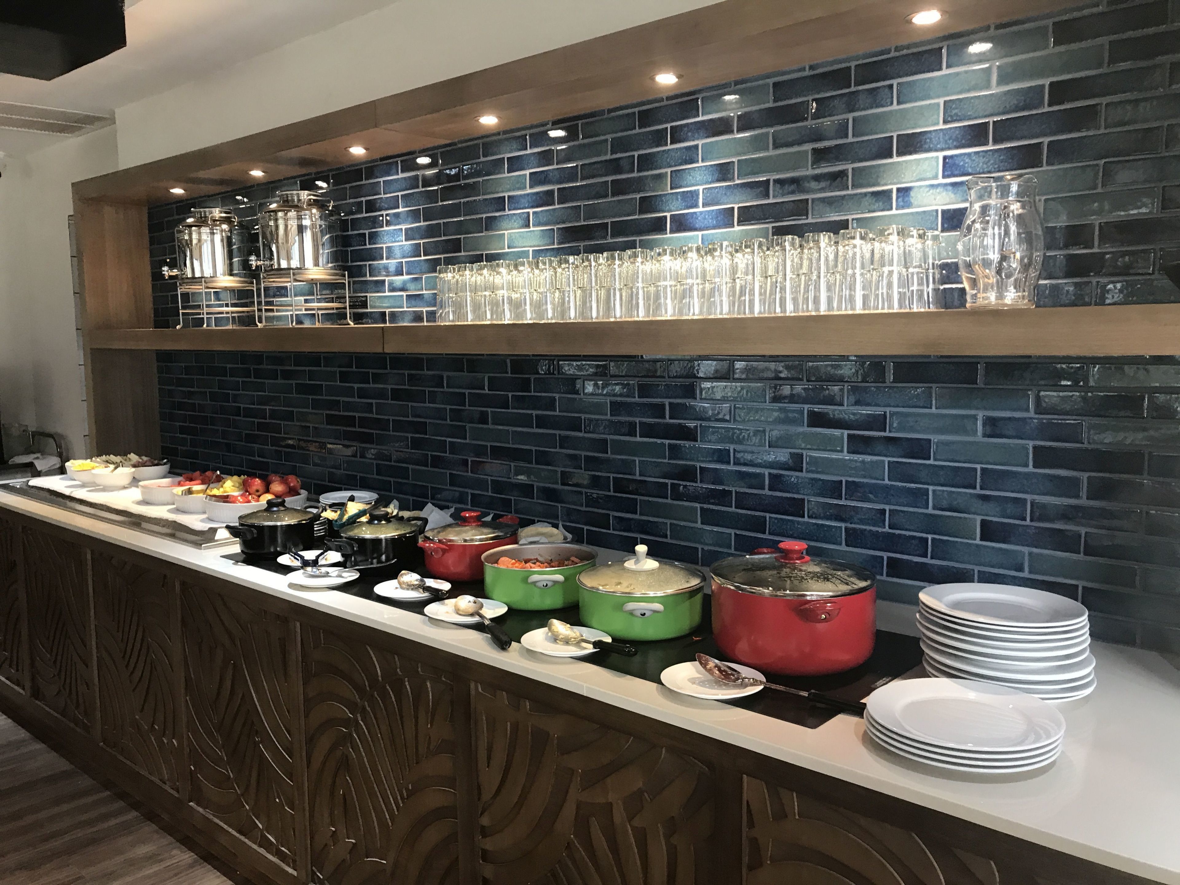 A buffet setup with various food items and glassware on a counter against a blue-tiled wall.