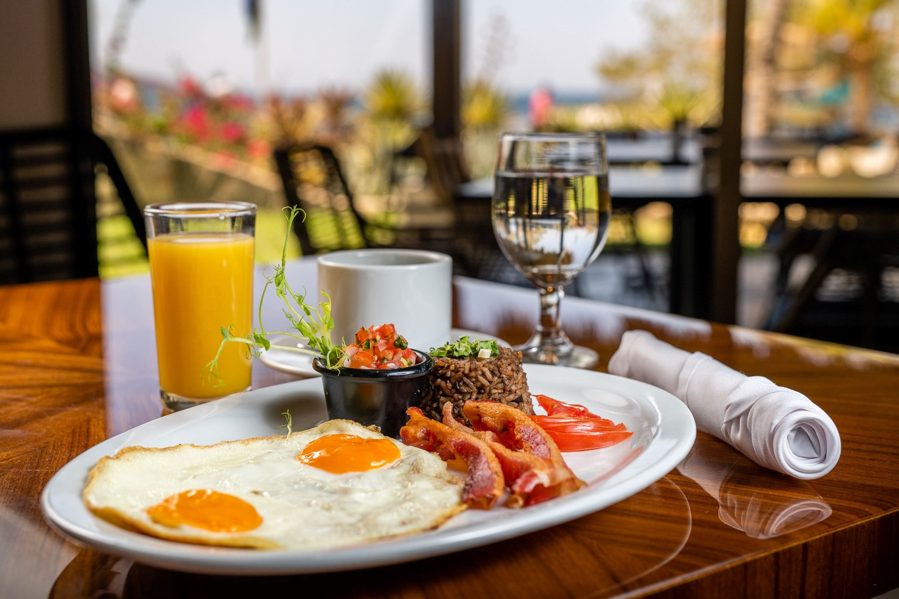 Une assiette de petit-déjeuner comprenant des œufs, du bacon et une portion de salsa, accompagnée d’un verre de jus d’orange et d’un verre d’eau.