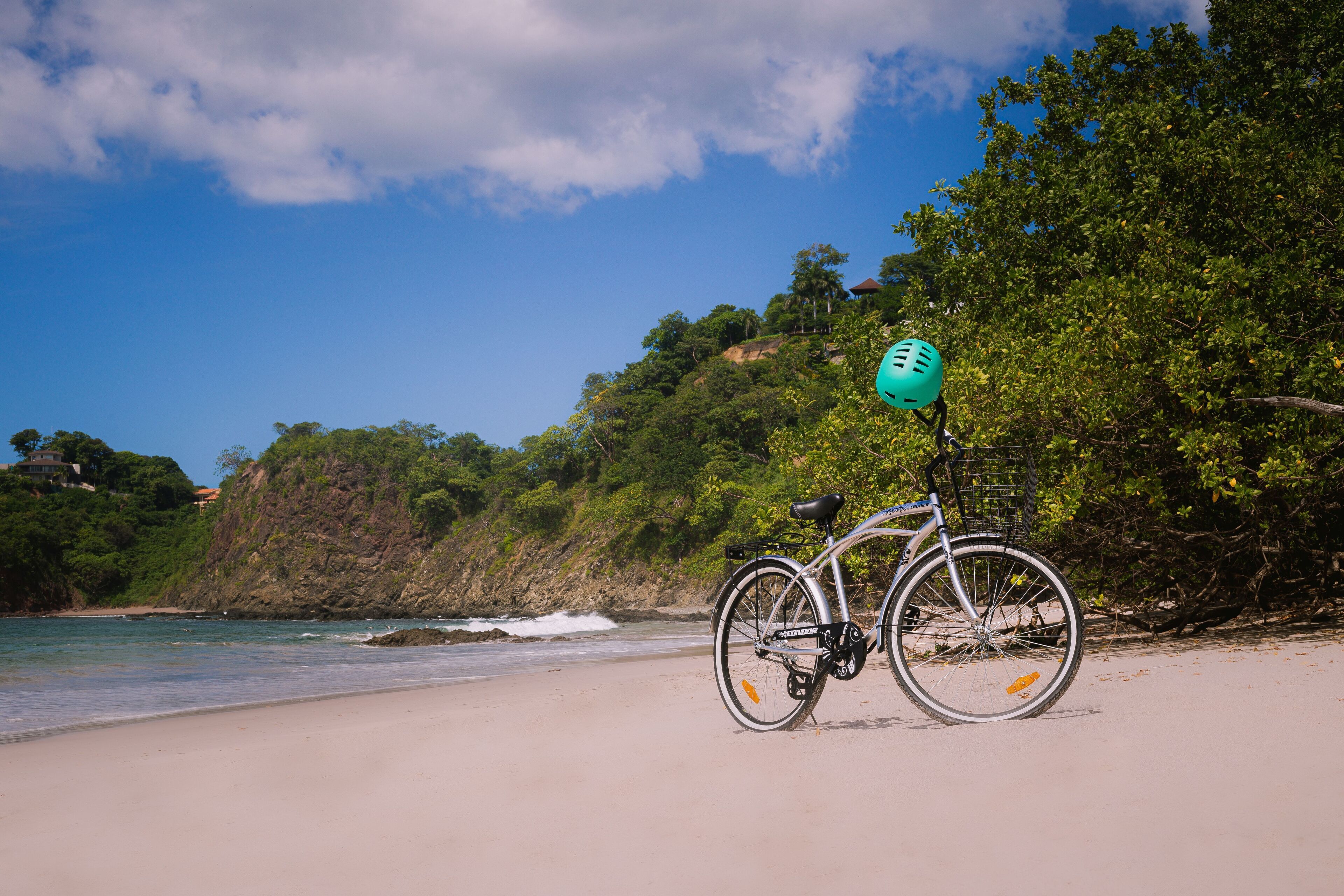 A bicycle parked on a sandy beach with a view of the ocean and a forested hillside.