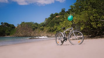 Een fiets geparkeerd op een zandstrand met uitzicht op de oceaan en een beboste heuvel.