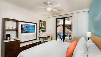 A hotel room with a bed, a desk, a chair, a ceiling fan, and a view of the outside.