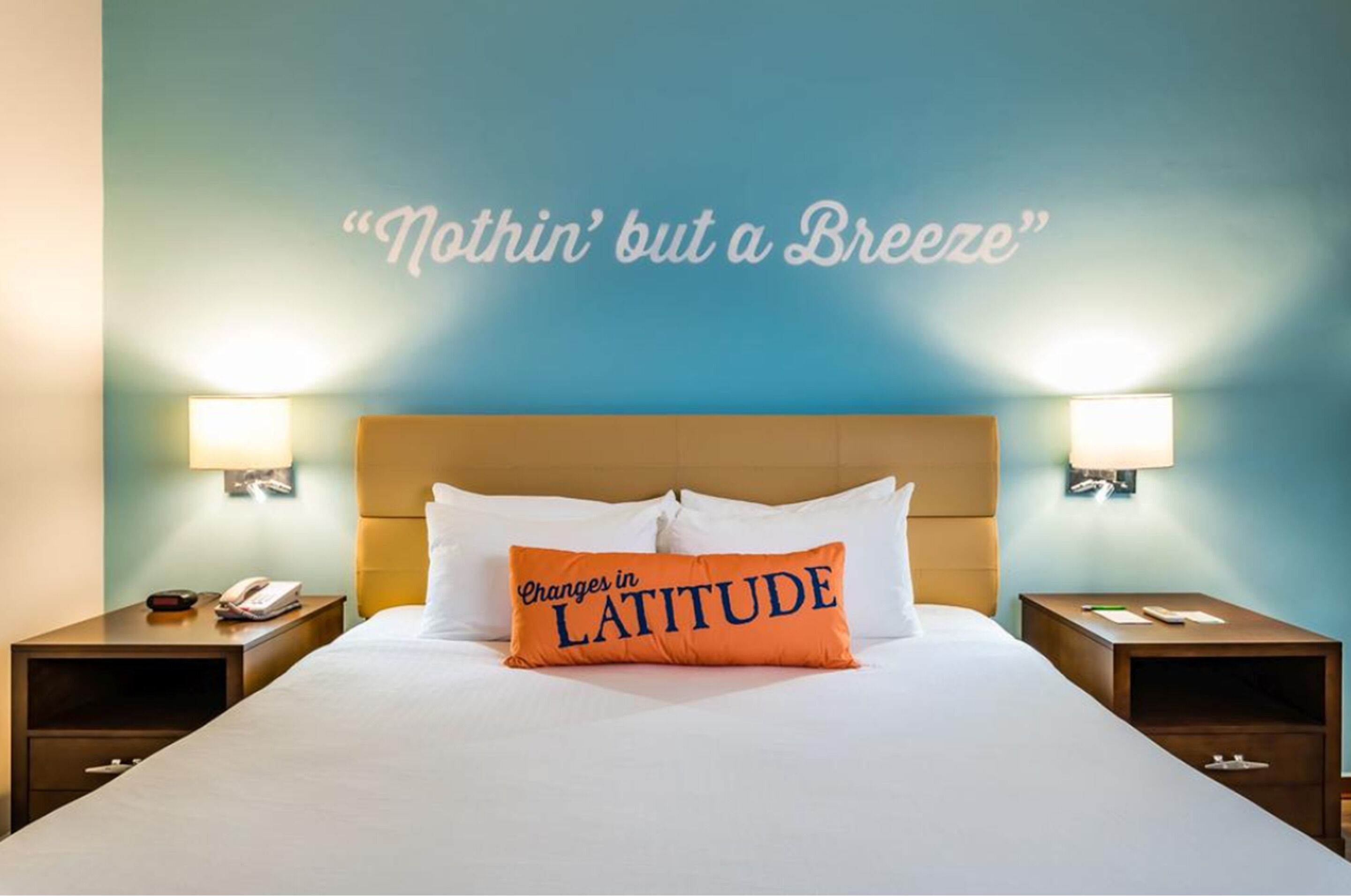 Una habitación de hotel con una cama, dos lámparas de noche y una pared con una cita.