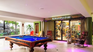 A pool table in a hotel lobby with a view of a tropical outdoor area.