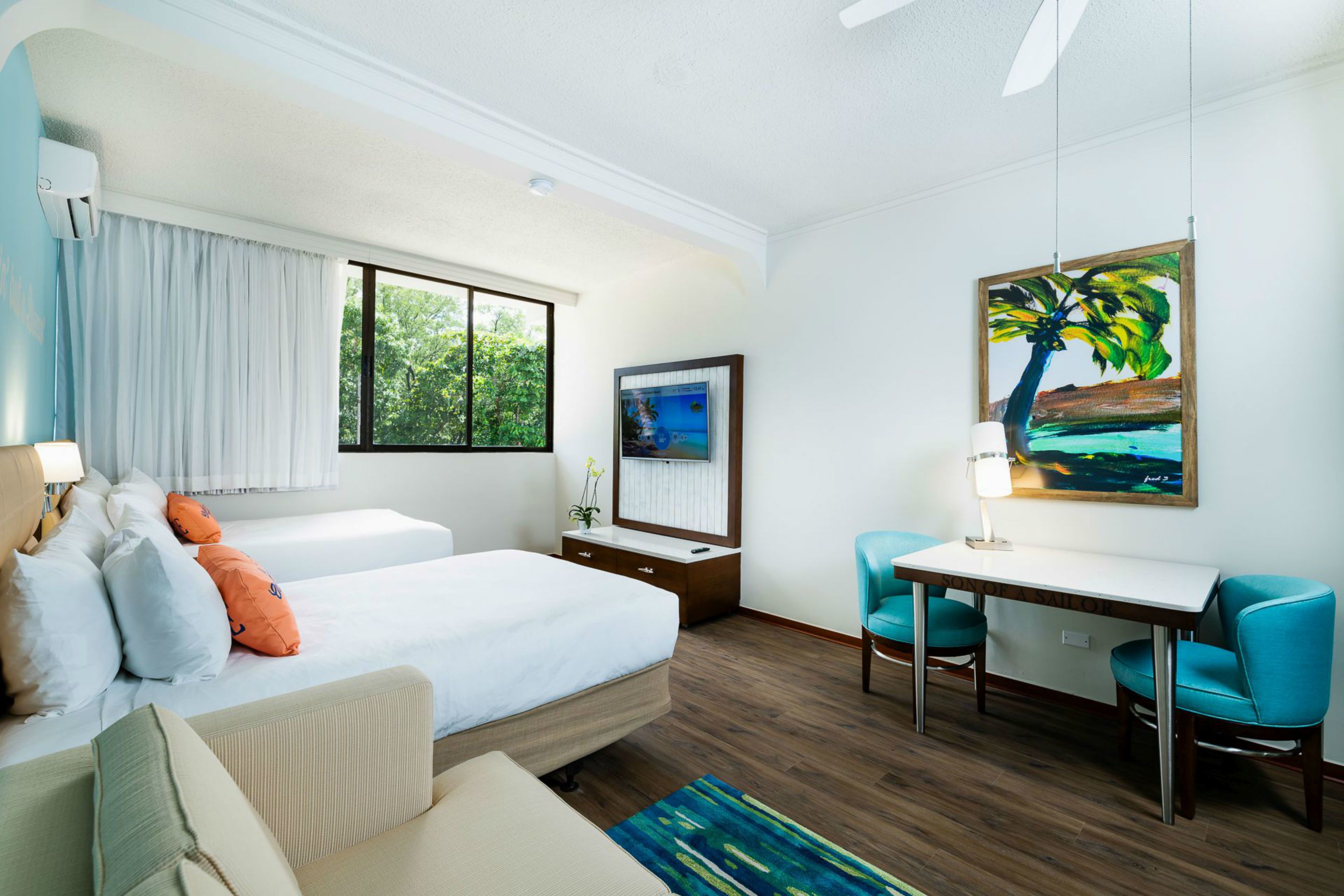 A hotel room with a bed, a desk, two chairs, a TV, and a painting.