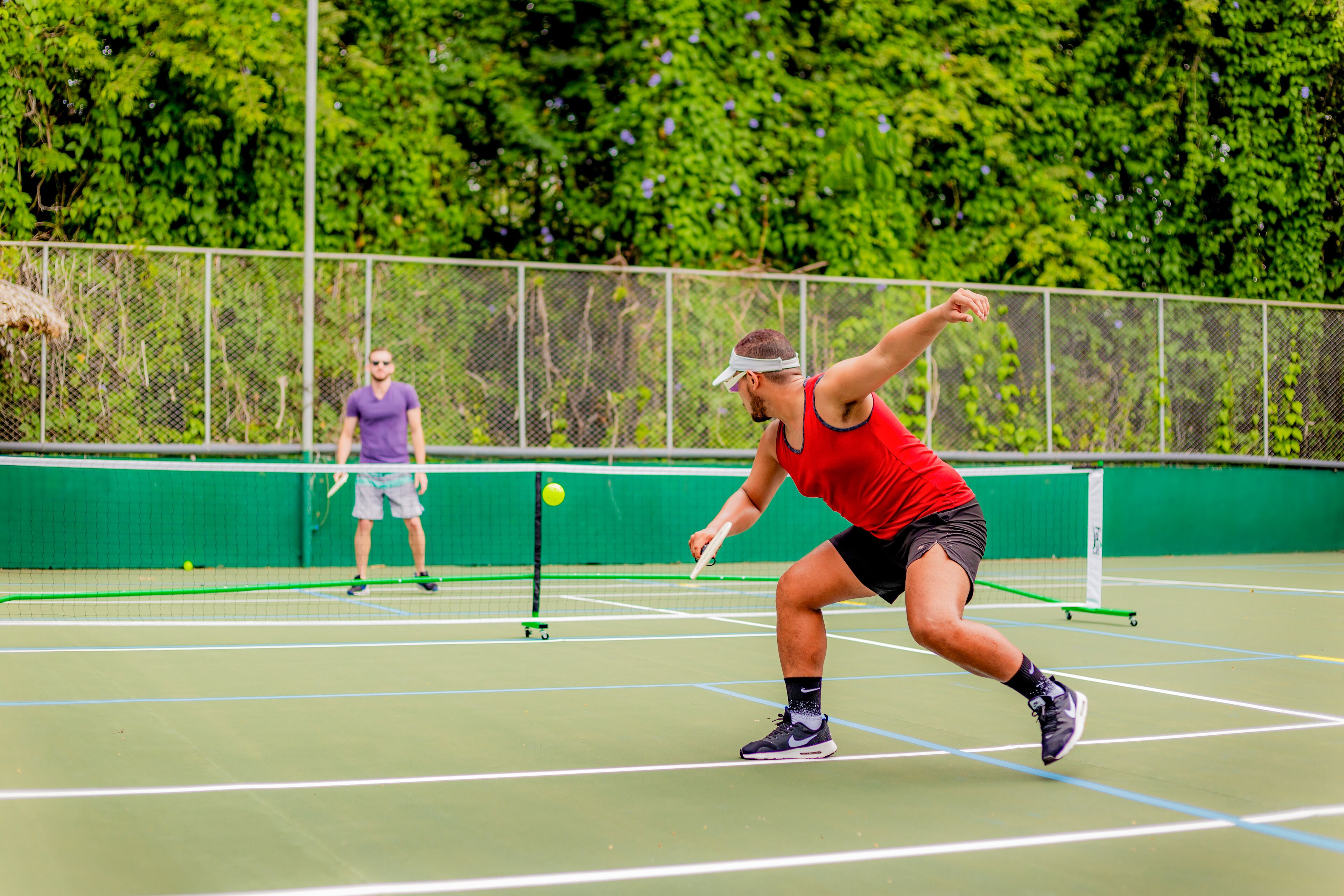 A tennis court with a net, a player in a red shirt, and another player in a purple shirt.