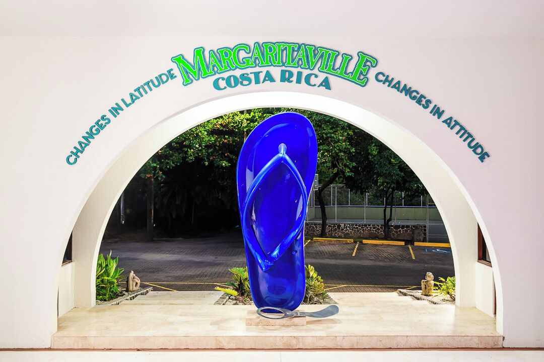 A blue glass sculpture under a sign that reads "Margaritaville Costa Rica" with the text "Changes in Latitude, Changes in Attitude" above it.