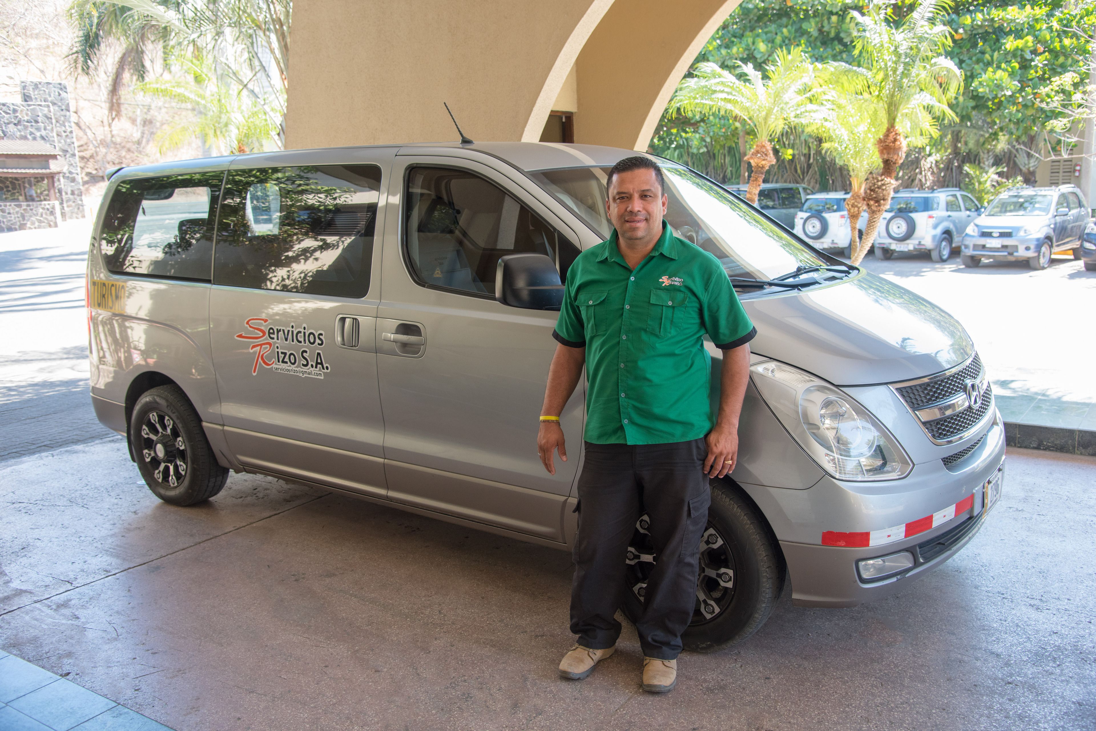 A man standing next to a silver van with "Servicios Rizo S.A" on the side.