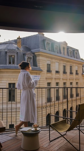 Eine Person liest eine Zeitung auf einem Balkon mit Blick auf ein historisches Gebäude.
