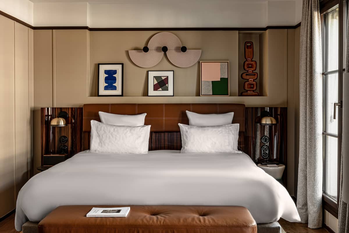 A large bed with white linens, two bedside tables with lamps, and artwork on the wall.
