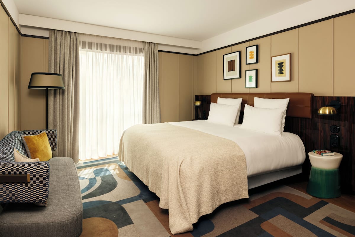 A hotel room with a large bed, a sofa, a lamp, and a small side table.