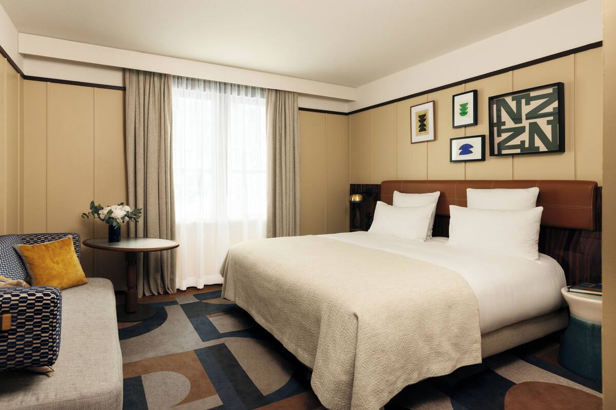 A hotel room with a large bed, a sofa, a small table with a vase, and a window with curtains.