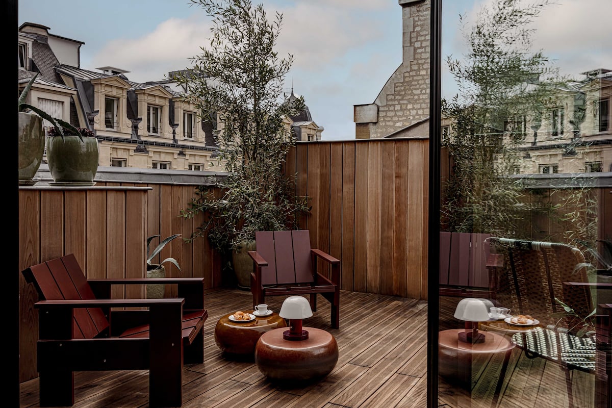 A wooden deck with a seating area, including chairs and round tables, overlooking a cityscape.