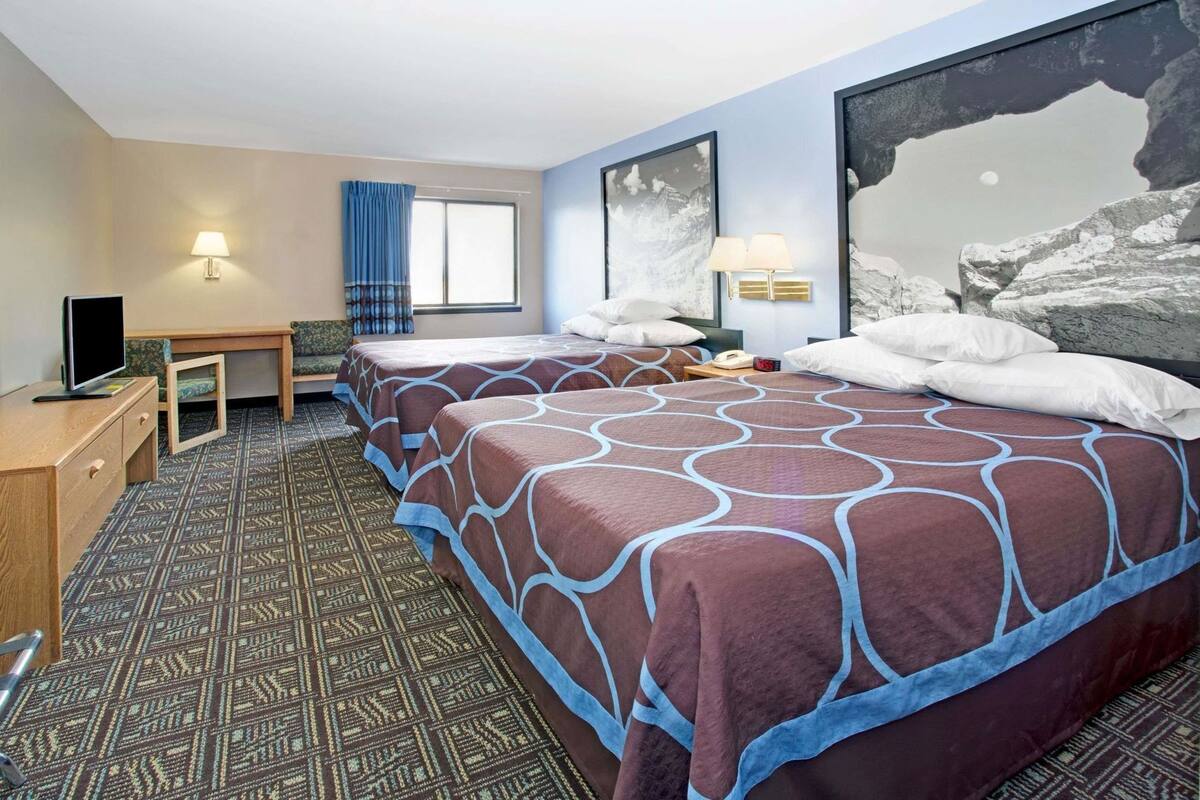 A hotel room with two beds, a desk, a TV, and a large window.