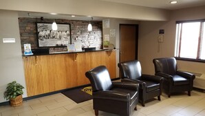 A reception area with a wooden counter, two leather chairs, a potted plant, and a framed welcome sign. - Super 8 by Wyndham Fort Collins (Fort Collins)