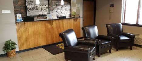 A reception area with a wooden counter, two leather chairs, a potted plant, and a framed welcome sign.