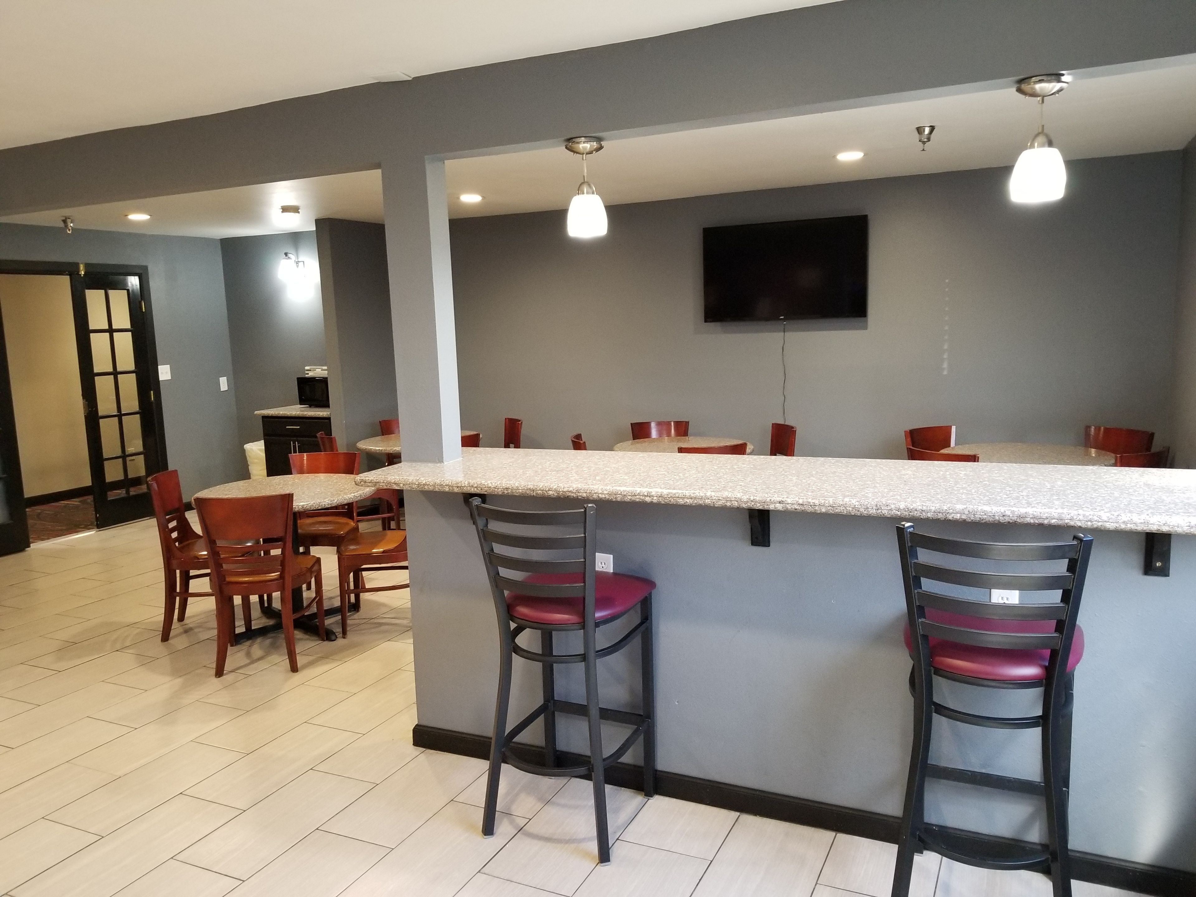A modern kitchen with a bar area, equipped with bar stools and a flat-screen TV mounted on the wall.