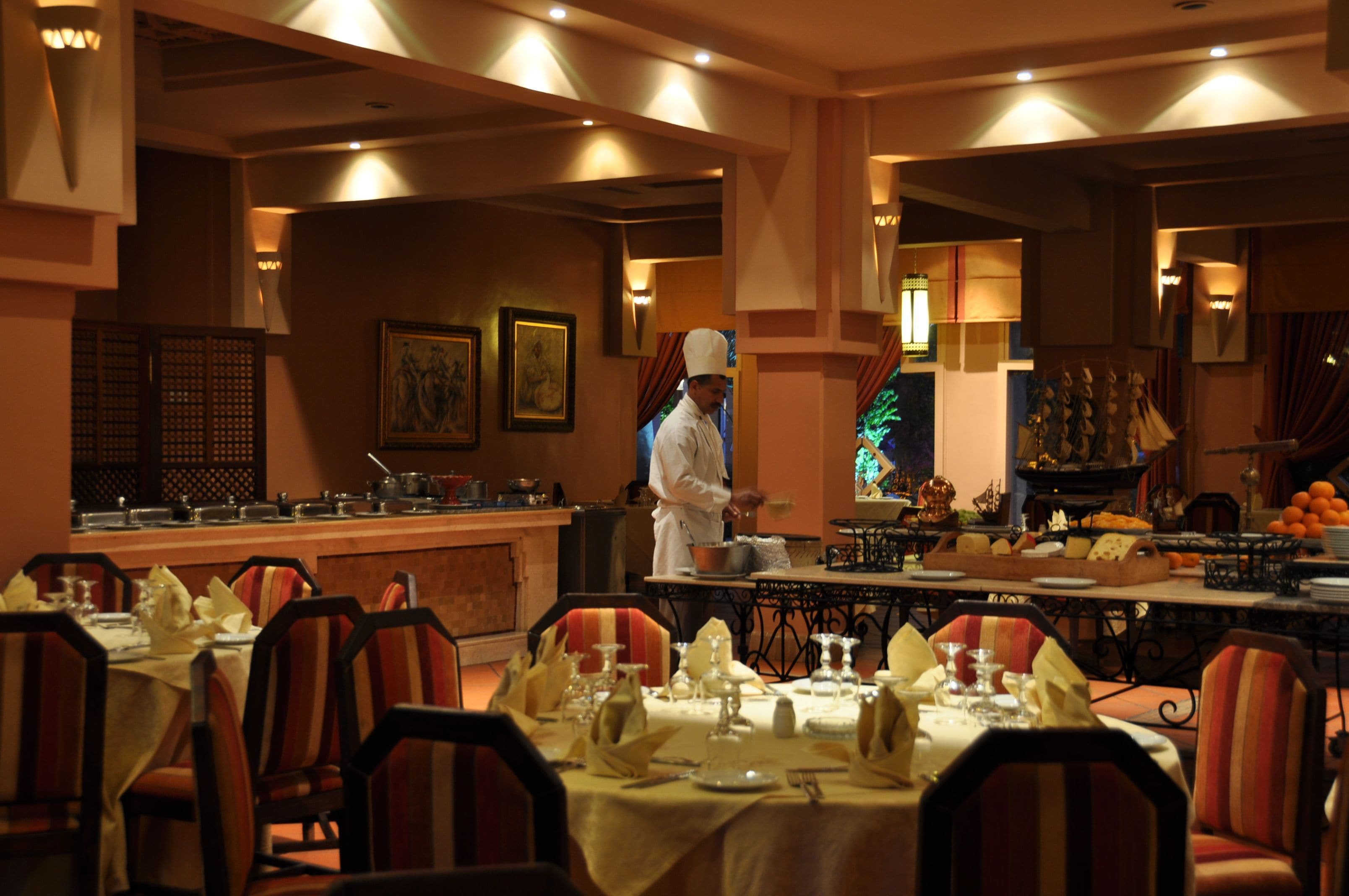 A restaurant with tables set for dining, a chef in the background, and a Christmas tree.
