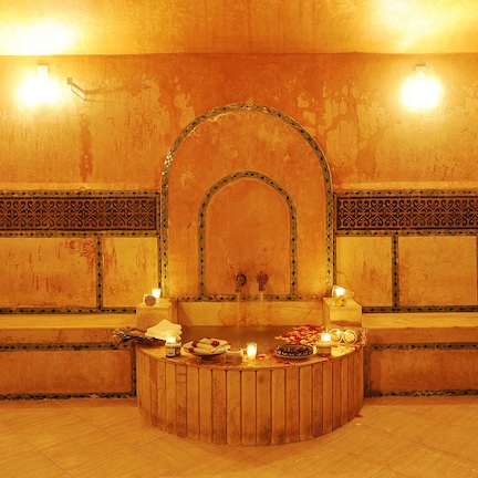 A spa room with a wooden bench, a small table with candles, and a decorative arch.