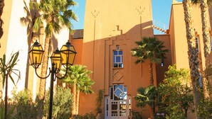 A building with a central entrance, palm trees, and a tiled pathway. - Le Berbere Palace (Ouarzazate)