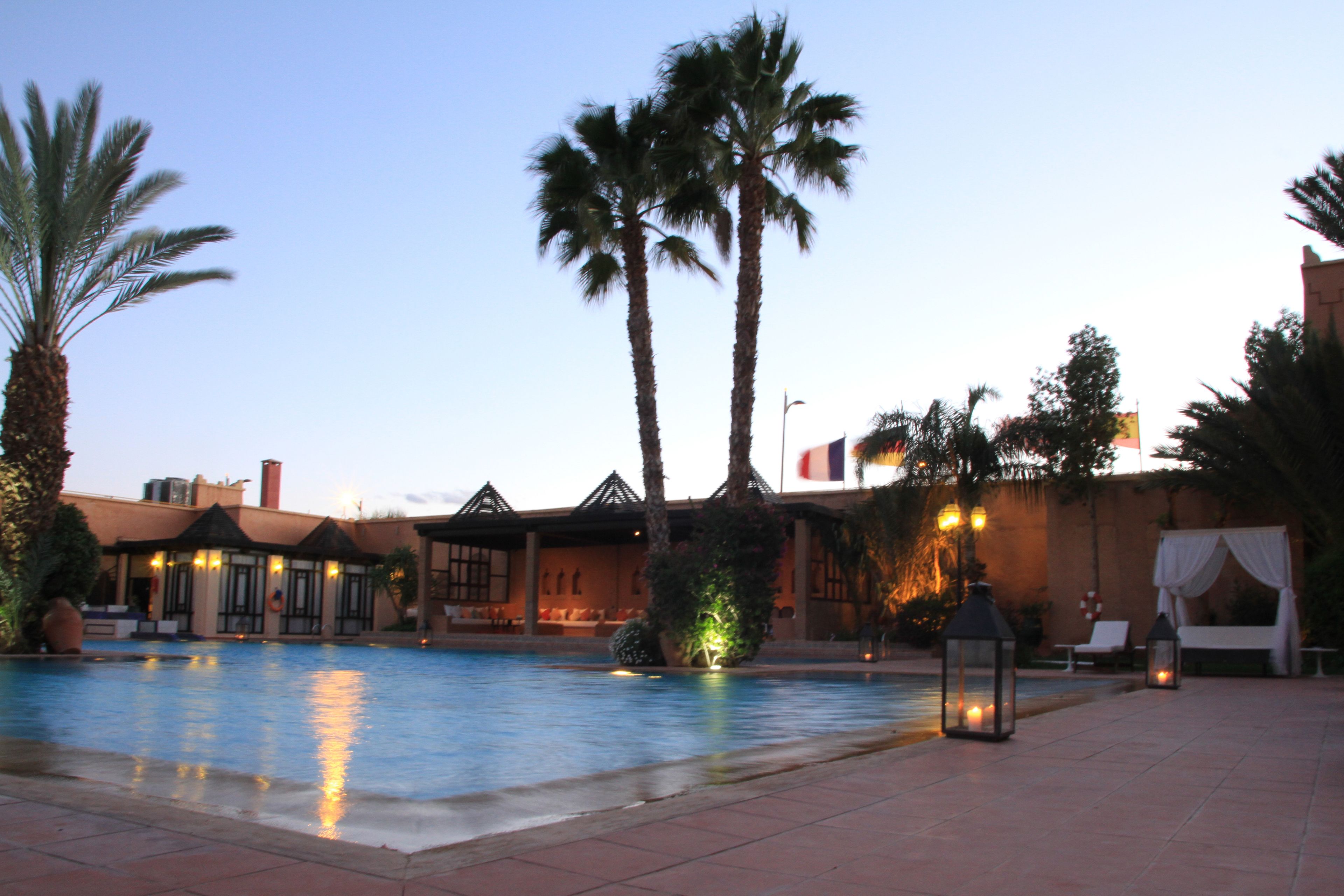 A pool area with a clear sky, palm trees, and a building with a tiled roof.