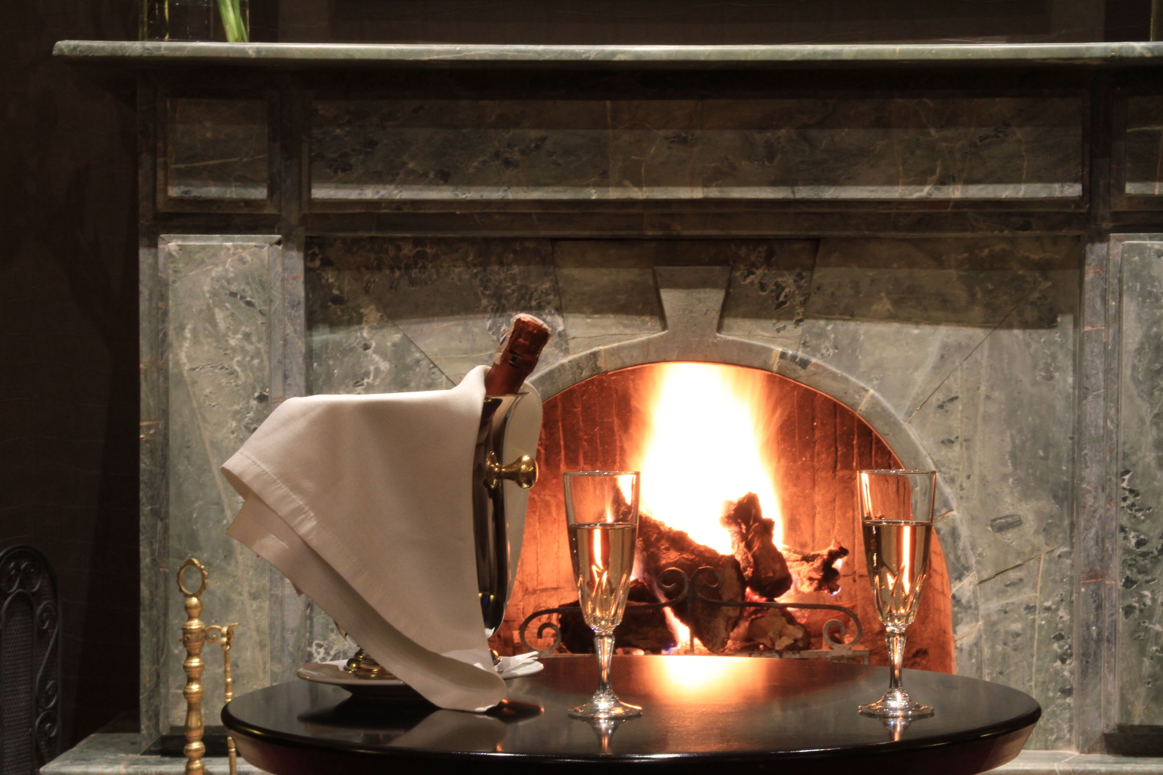 A fireplace with a table in front, a bottle, and two glasses.
