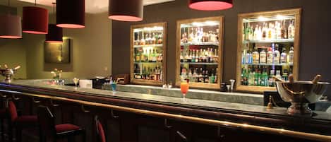 Zona de bar con varias botellas de licor, una barra y taburetes rojos.