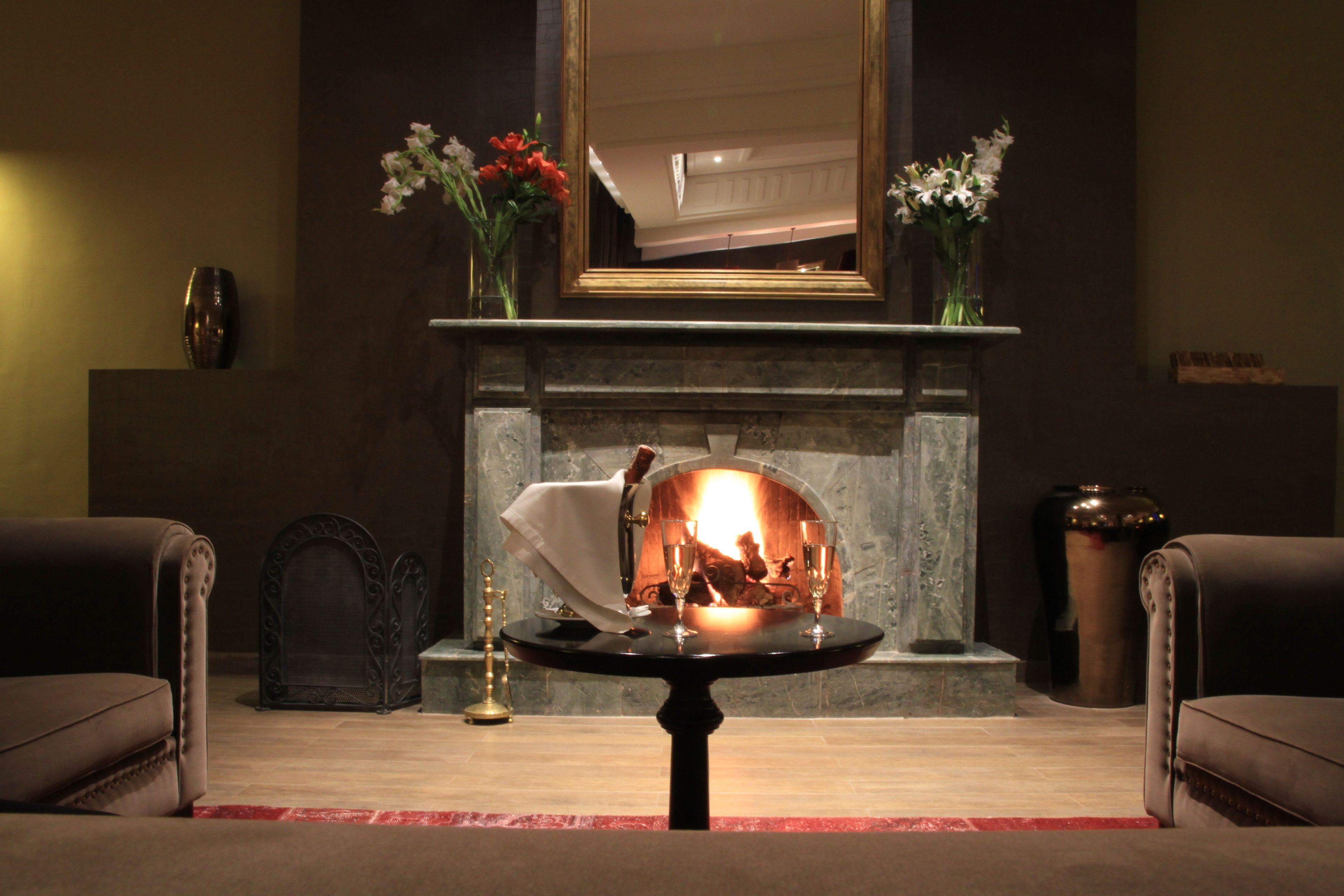 A cozy room with a fireplace, two armchairs, a table with glasses, and vases with flowers.