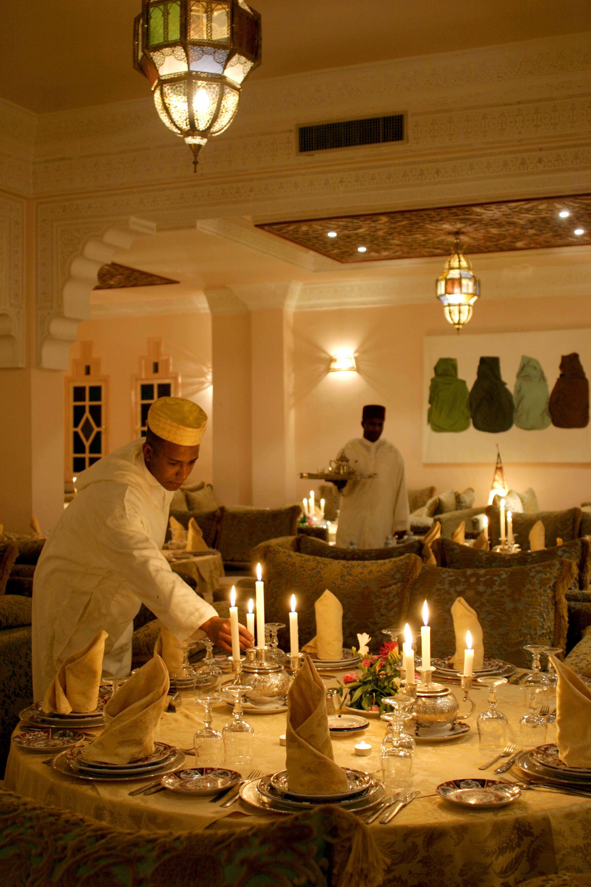 A dining area with a table set for a meal, candles, and a waiter attending to the table.