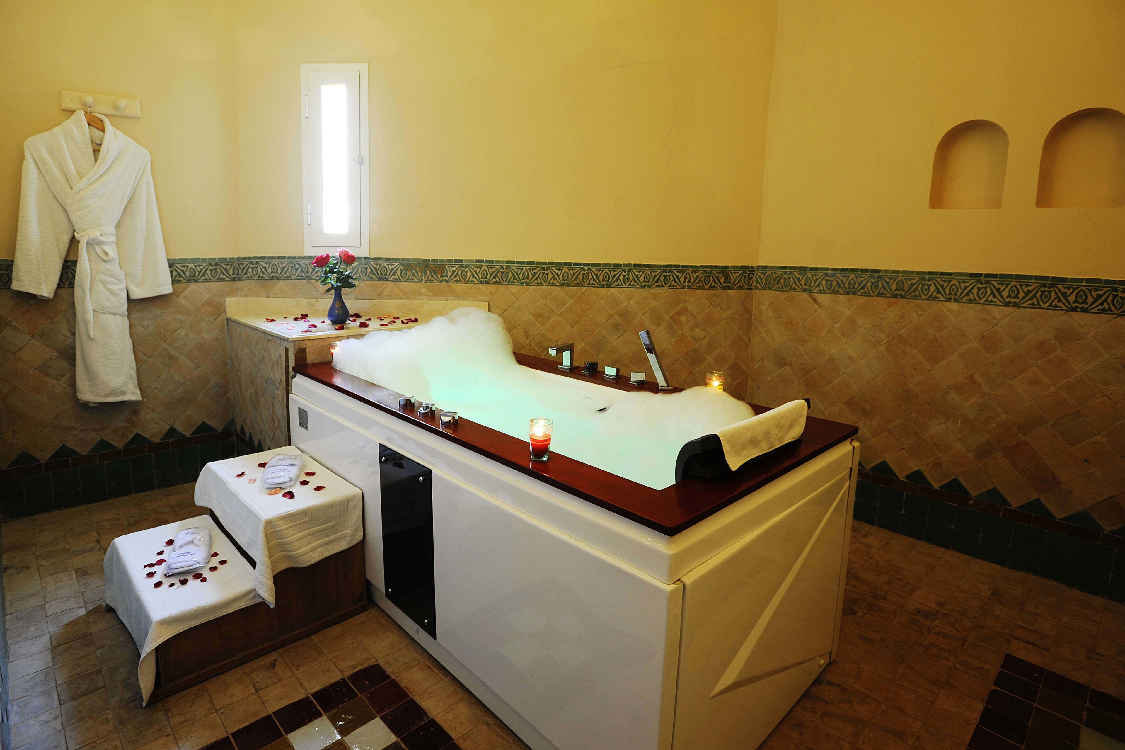 A spa room with a bathtub, a towel rack, and a small table with a vase of flowers.