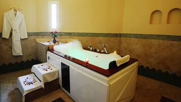 A spa room with a bathtub, a towel rack, and a small table with a vase of flowers.