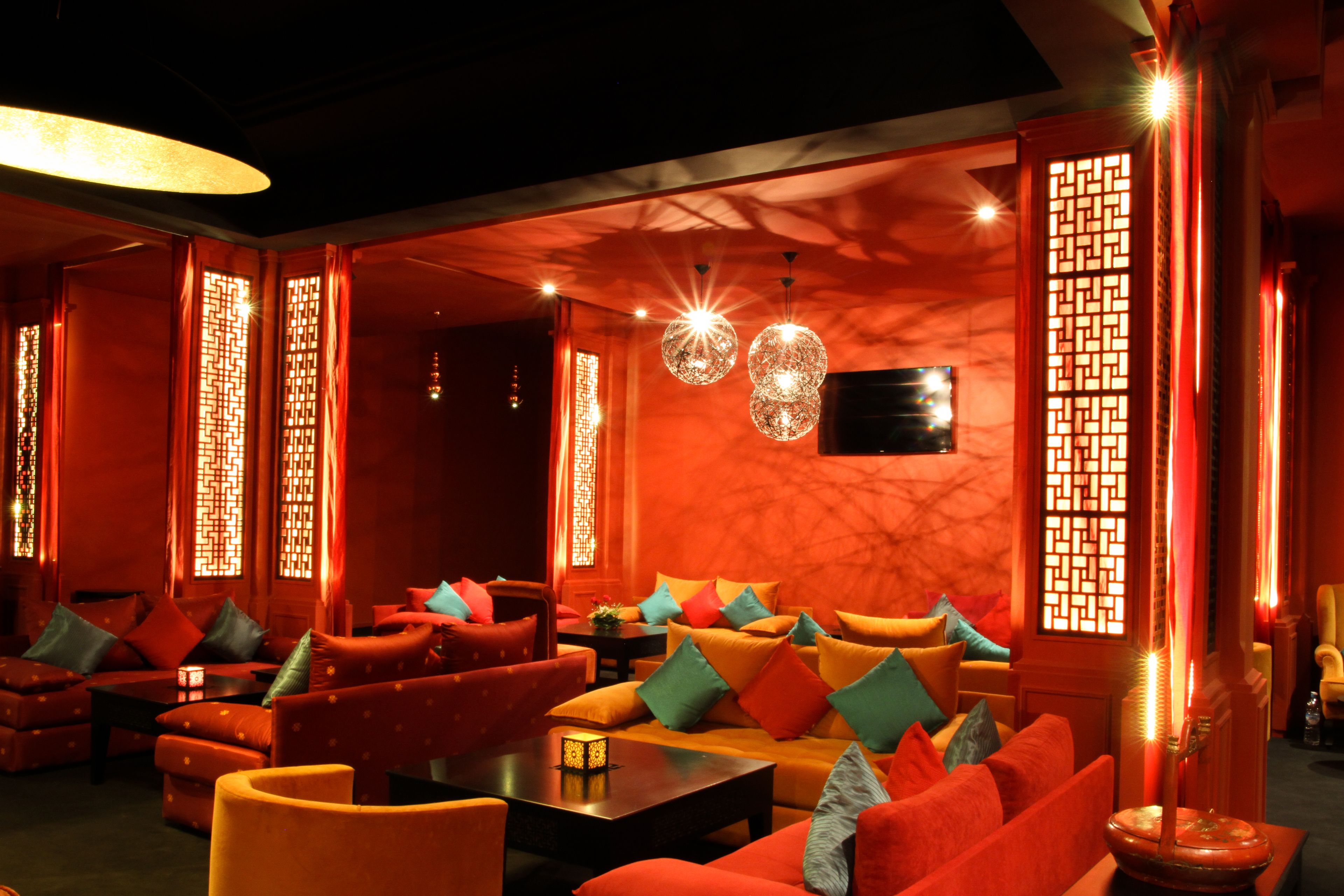 Ein gemütlich beleuchteter Lounge-Bereich mit Rot- und Orangetönen, mit Sofas, einem Couchtisch und dekorativer Beleuchtung.