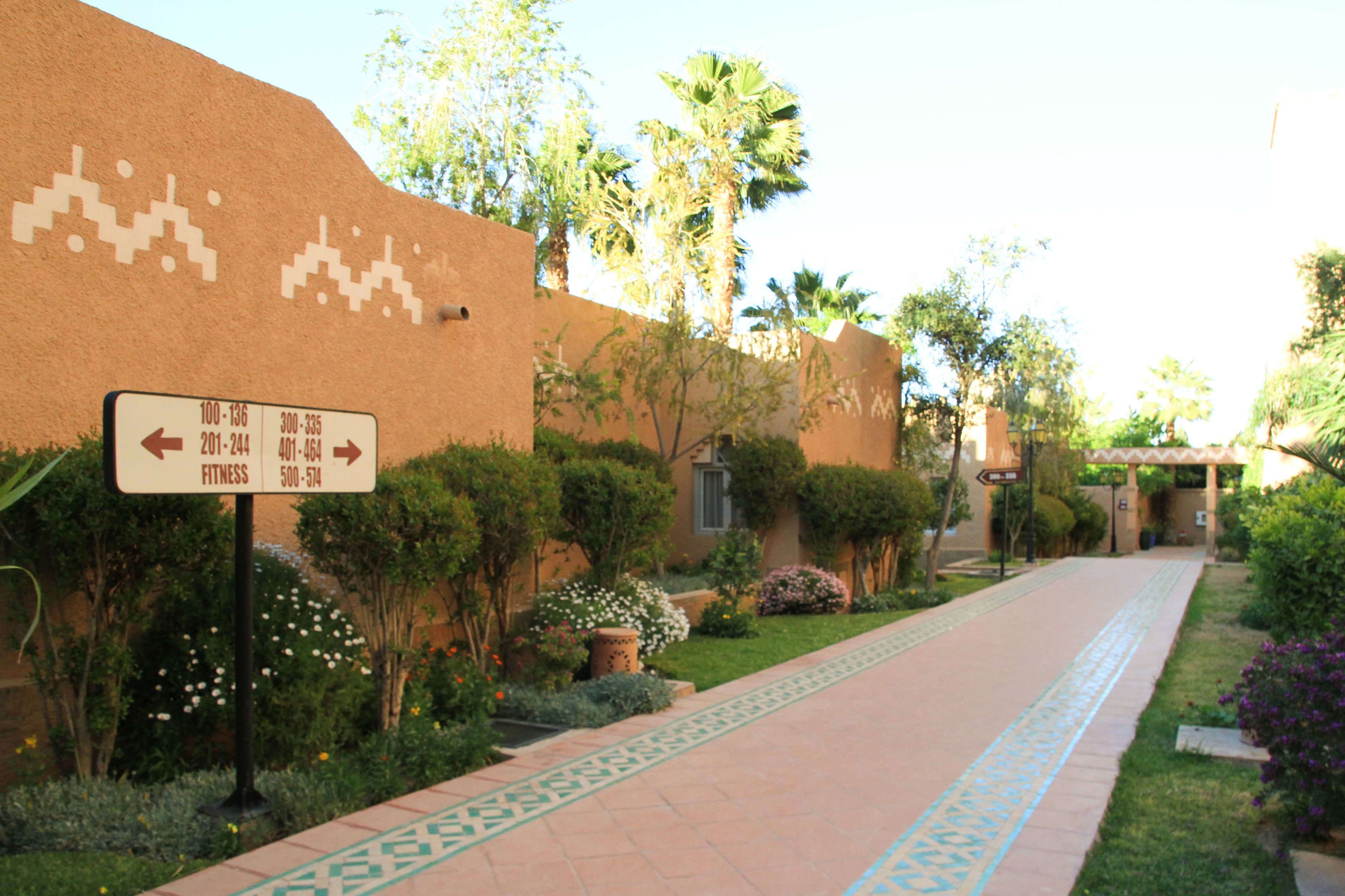 A pathway with directional signs, surrounded by greenery and palm trees.