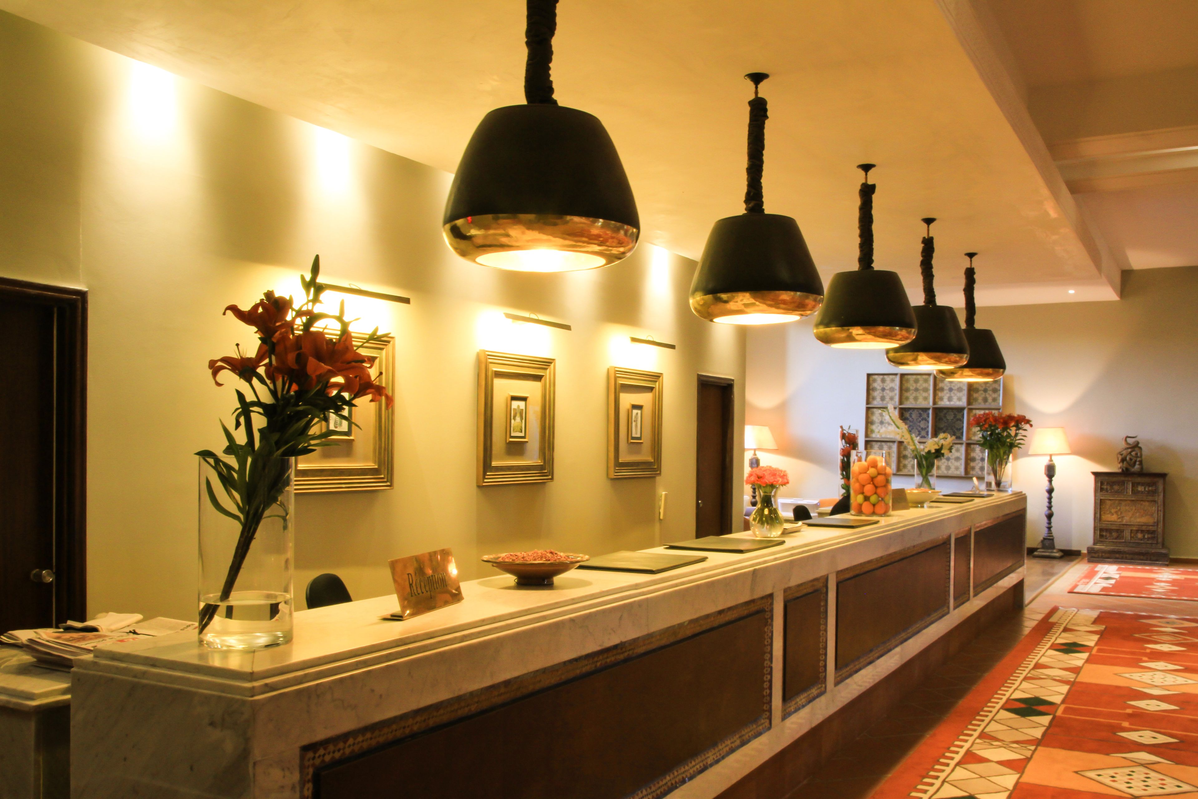 A hotel reception area with a marble counter, framed pictures on the wall, and hanging pendant lights.