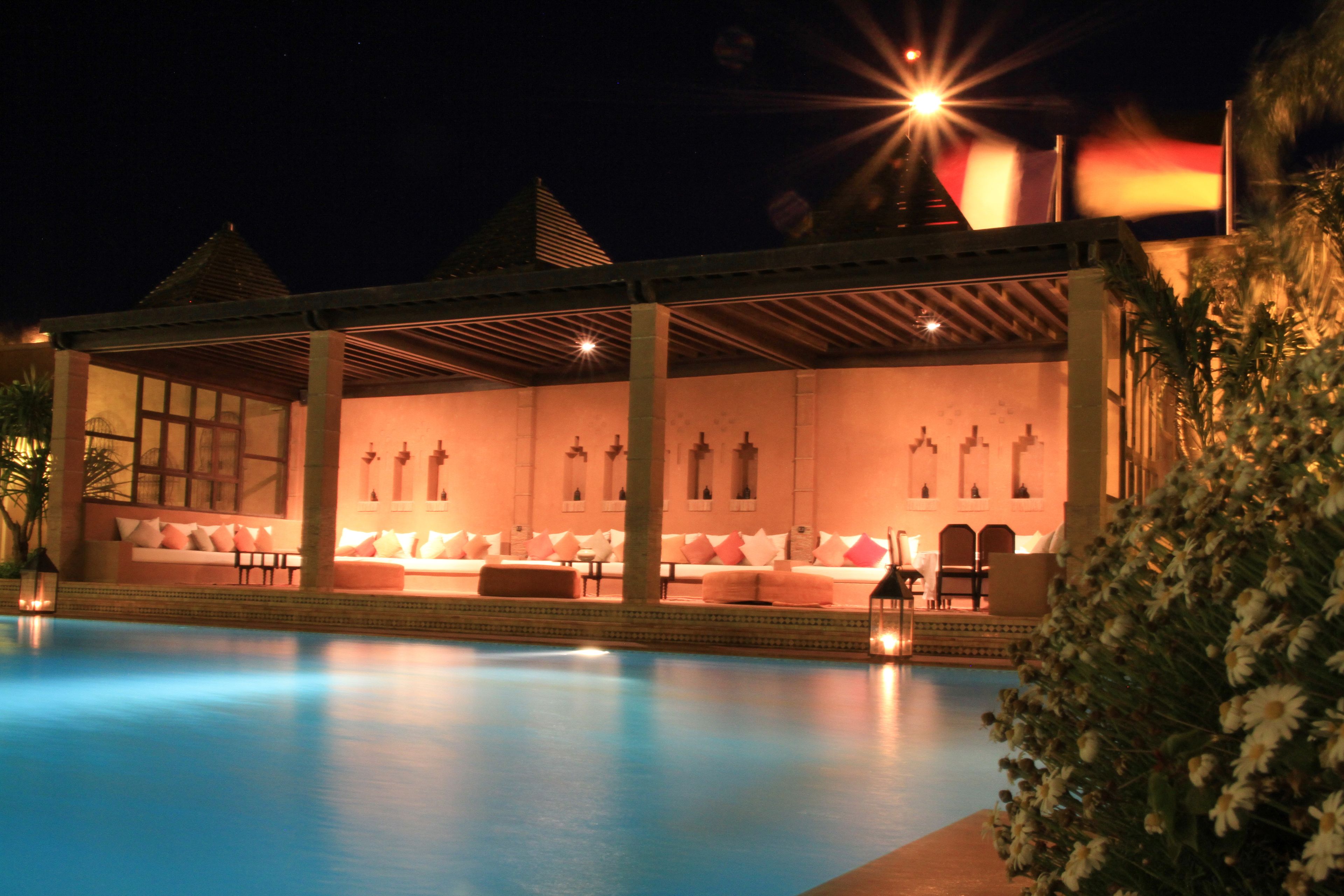 Zona junto a la piscina con un área de estar cubierta, piscina y cielo nocturno.