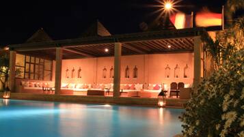 Zona junto a la piscina con un área de estar cubierta, piscina y cielo nocturno.