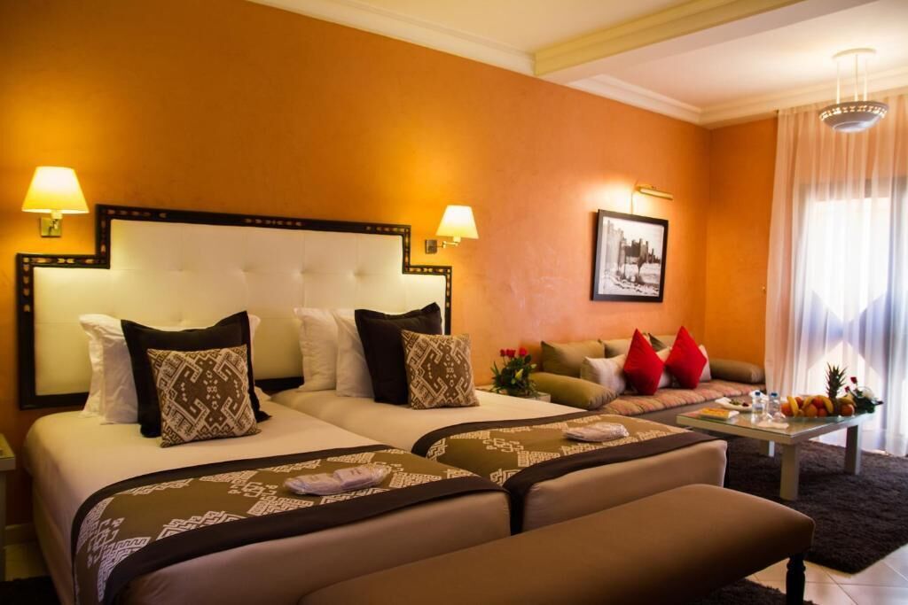 A hotel room with two beds, a sofa, a coffee table, and a cityscape picture on the wall.