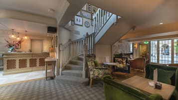 A hotel lobby with a staircase, seating area, and a reception desk.