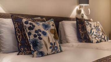 A neatly made bed with floral-patterned pillows and a wall-mounted lamp.