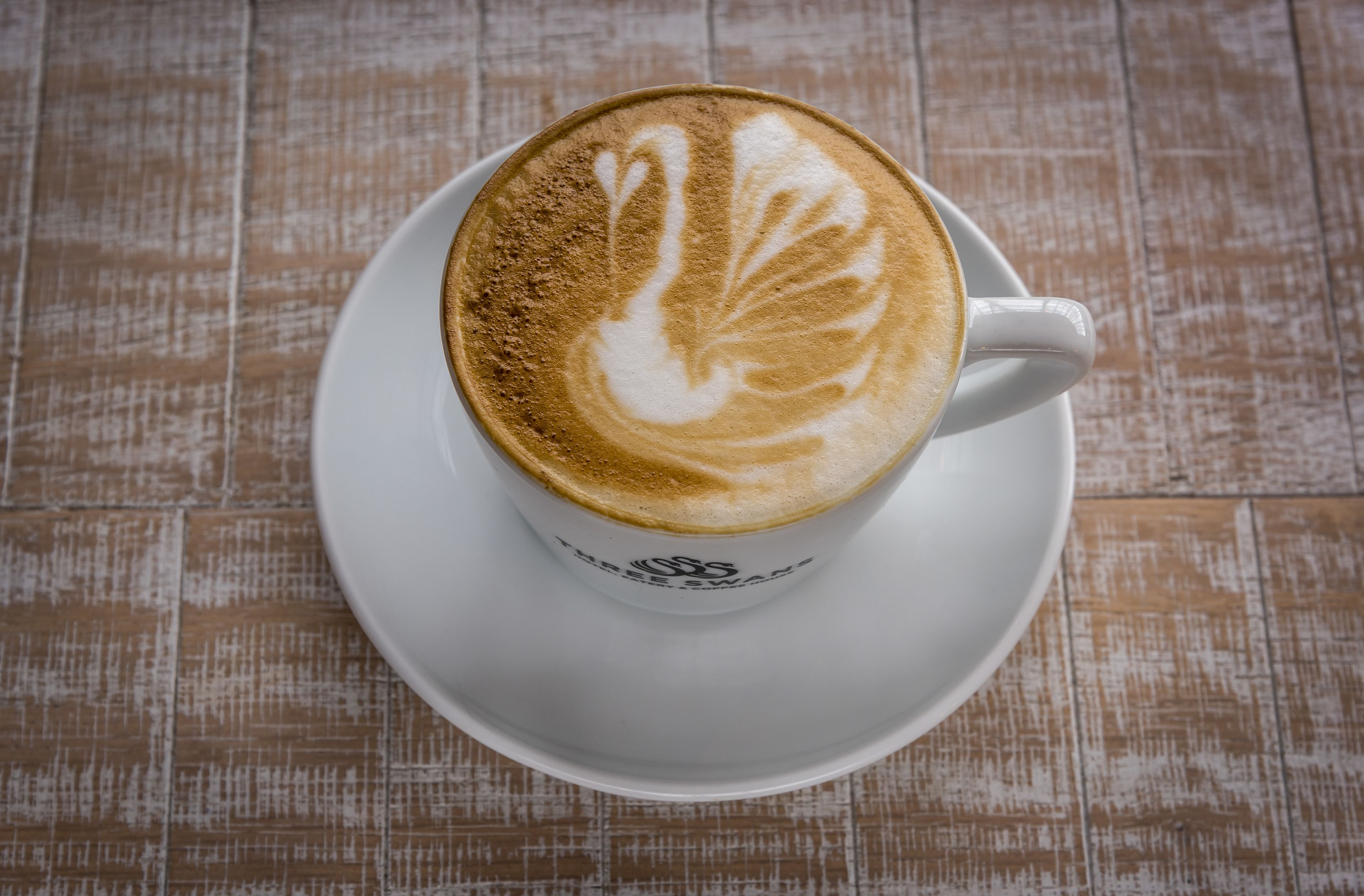 Une tasse de café surmontée d’un motif en latte, posée sur une soucoupe blanche.