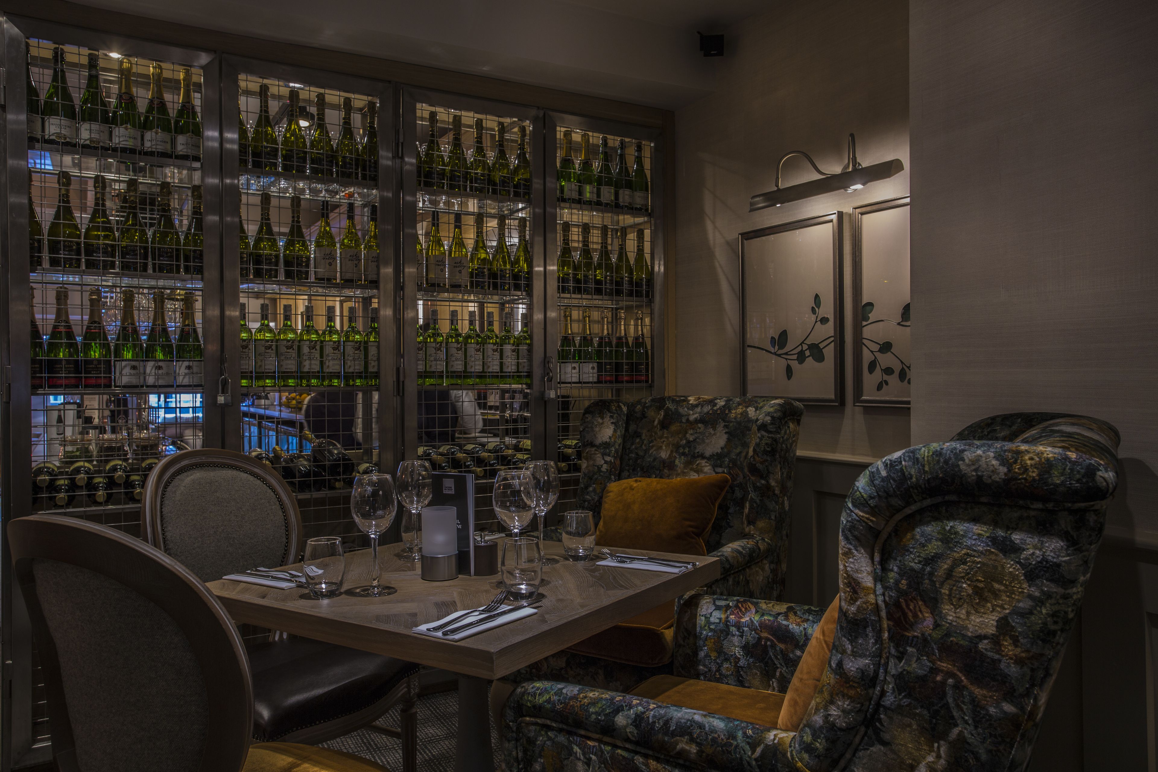 A dining area with a table set for two, surrounded by patterned chairs, and a wine rack in the background.