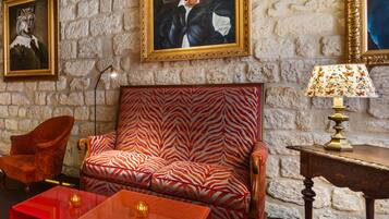 A room with a zebra-patterned sofa, a red armchair, a wooden side table with a lamp, and framed artwork on the walls.