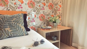Una cama bien hecha con una almohada estampada, un par de gafas de sol y un libro titulado