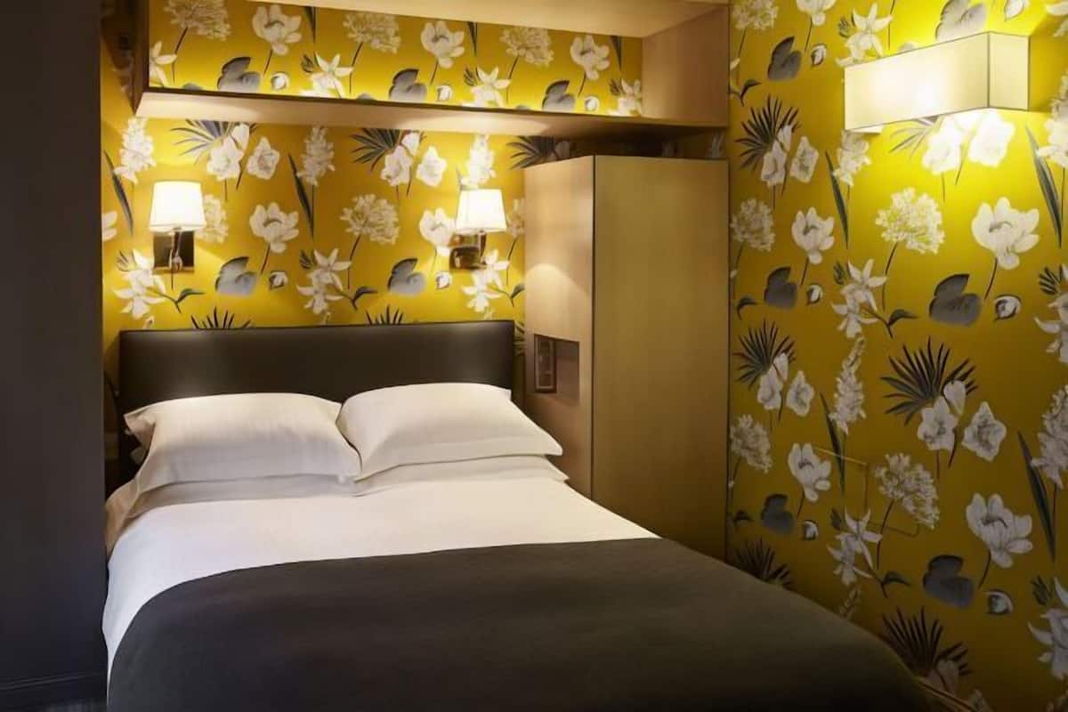 Ein Hotelzimmer mit einem Bett, einem Kleiderschrank und einer Wand mit Blumenpapier.