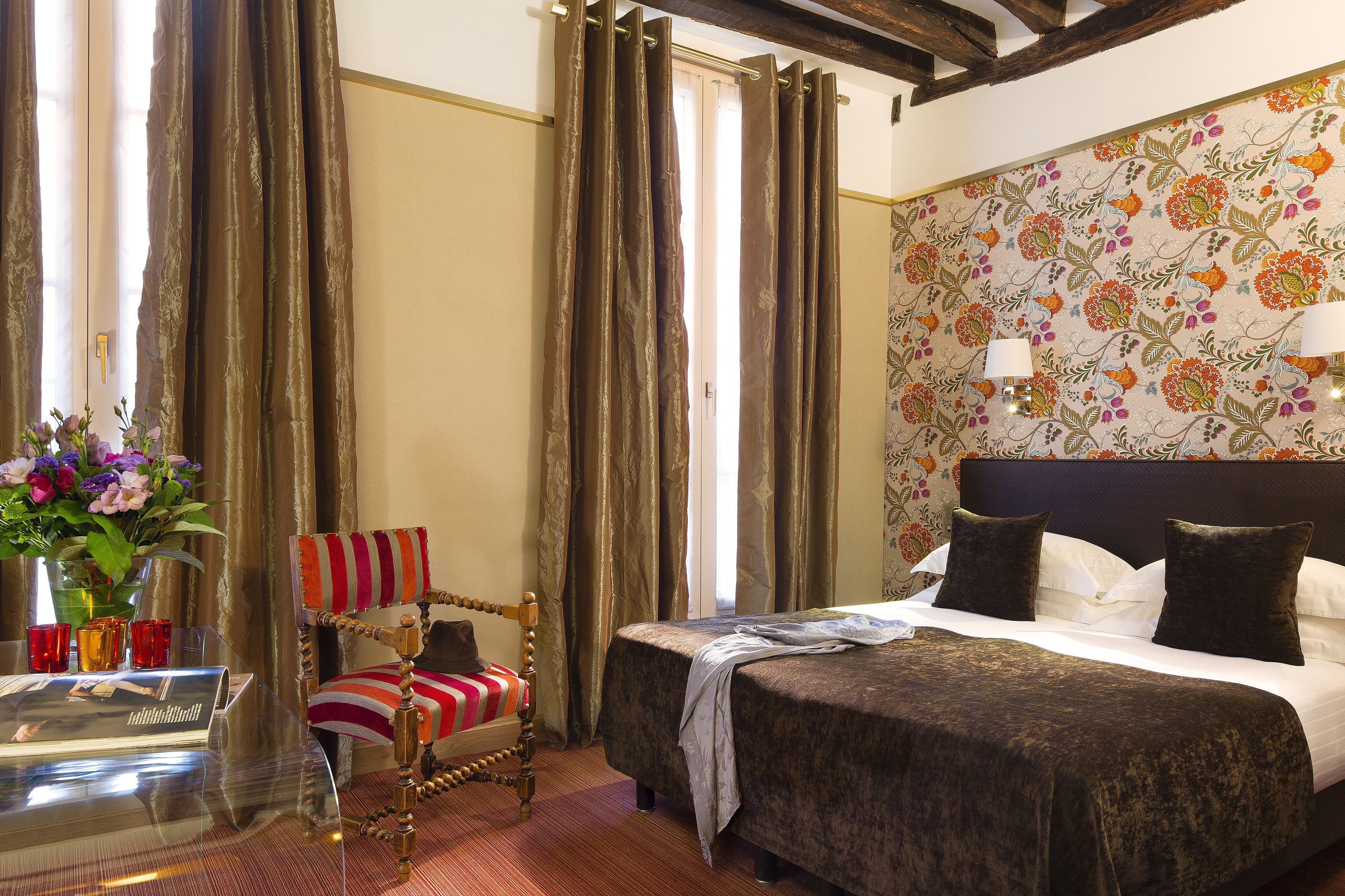Quarto de hotel com cama, cadeira, mesa e um vaso de flores, além de cortinas.