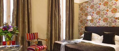 Quarto de hotel com cama, cadeira, mesa e um vaso de flores, além de cortinas.