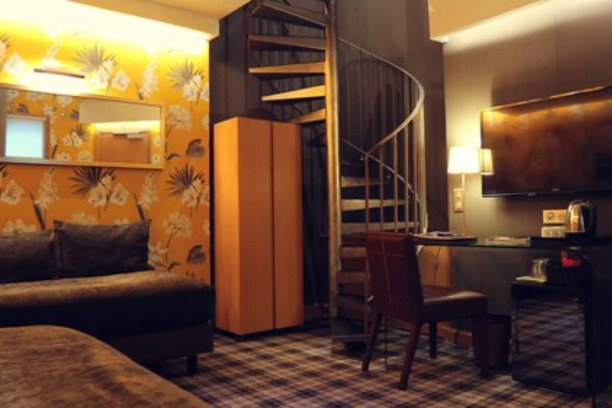 Ein Hotelzimmer mit Sofa, Schreibtisch, Stuhl, Wendeltreppe und Fernseher.
