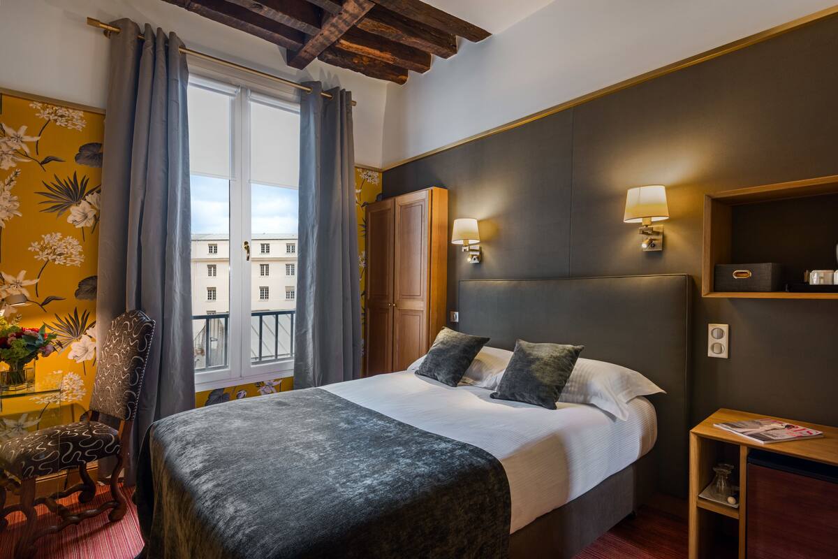 Ein Hotelzimmer mit einem großen Bett, einem hölzernen Kopfteil, einem Nachttisch, einer Lampe und einem Fenster mit Vorhängen.